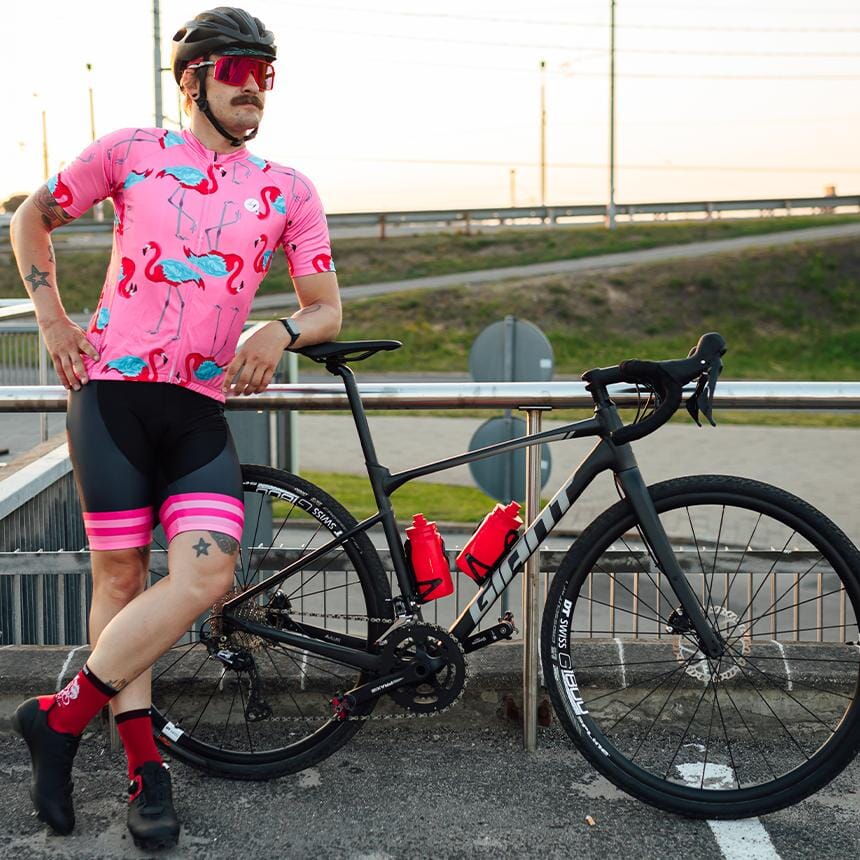 a man in a pink shirt with a flamingo pattern is standing next to a bike